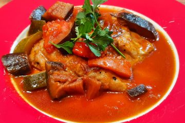 A plate of pepperonata sauce with eggplant, tomatoes with chicken and garnished with parsley