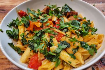 A bowl of penne pasta with spicy sausage, cherry tomatoes and garnished with fresh basil and parsley