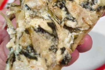 A slice of artichoke and spinach pizza held by hand