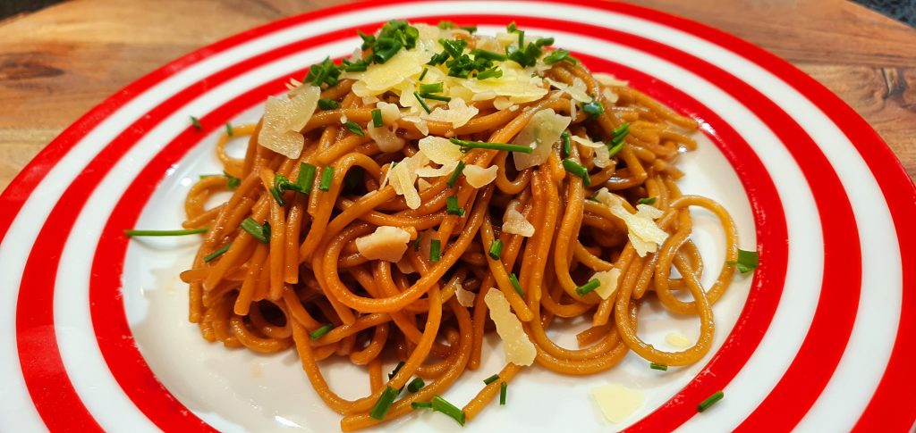 Vegemite spaghetti served on a plate garnished with parmesan and chives